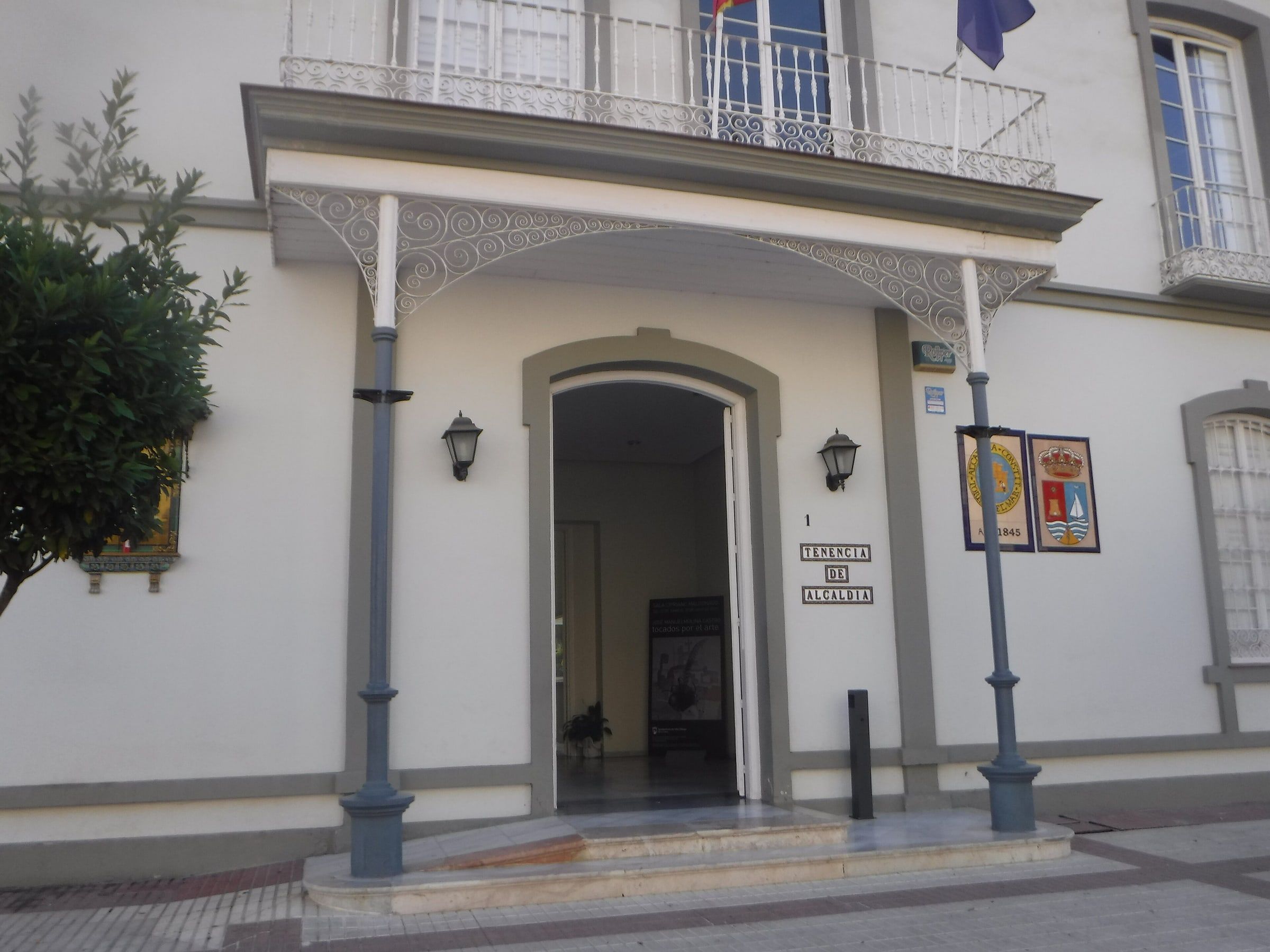Entrada de la Casa Larios de Torre del Mar, sede de la tenencia de alcaldía, con el balcón de las banderas sobre la puerta y los escudos junto al portal