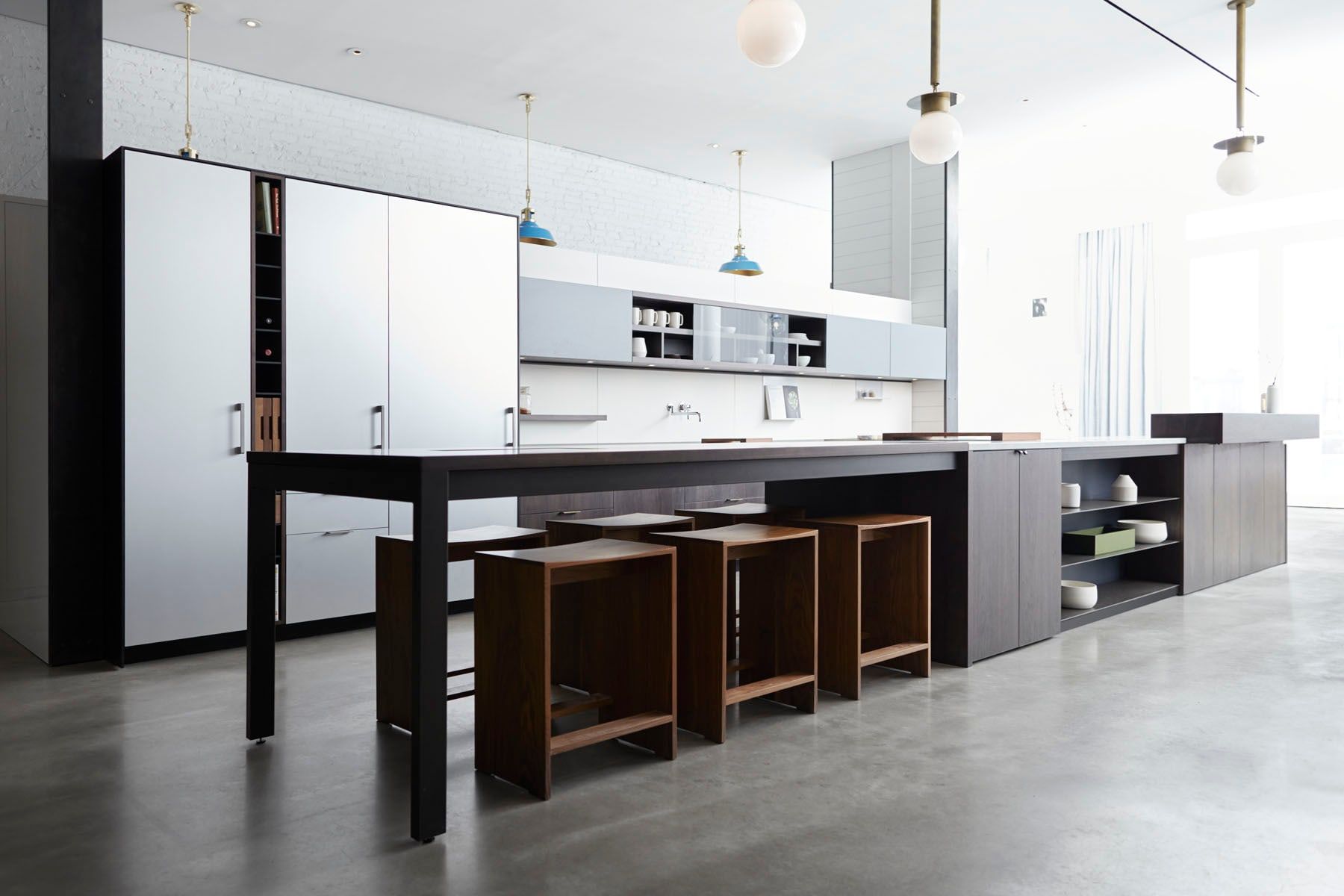 Cocina moderna de exposición con isla central de estructura negra, taburetes de madera, muebles blancos y lámparas colgantes