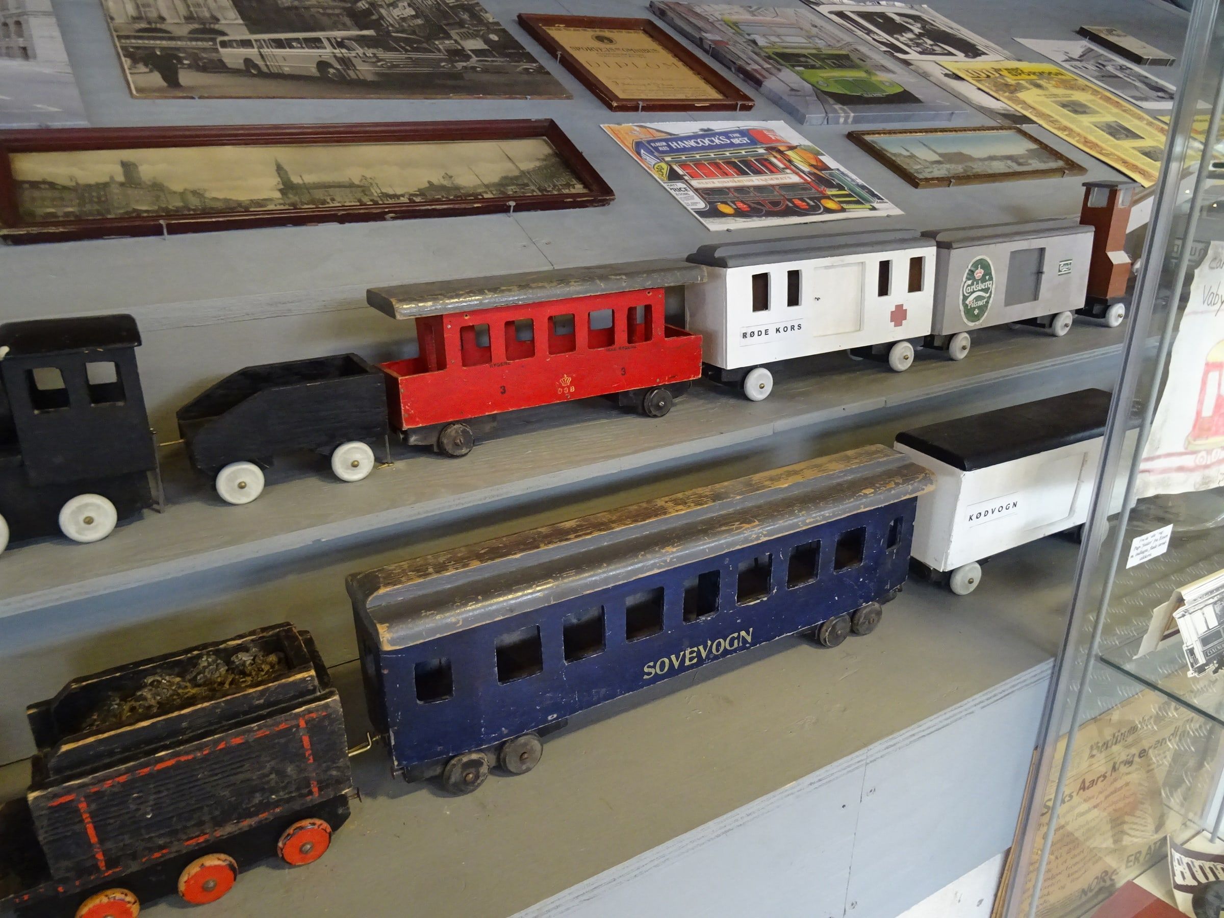 Trenes de juguete de madera pintados de colores, con locomotora y vagones, expuestos en una vitrina