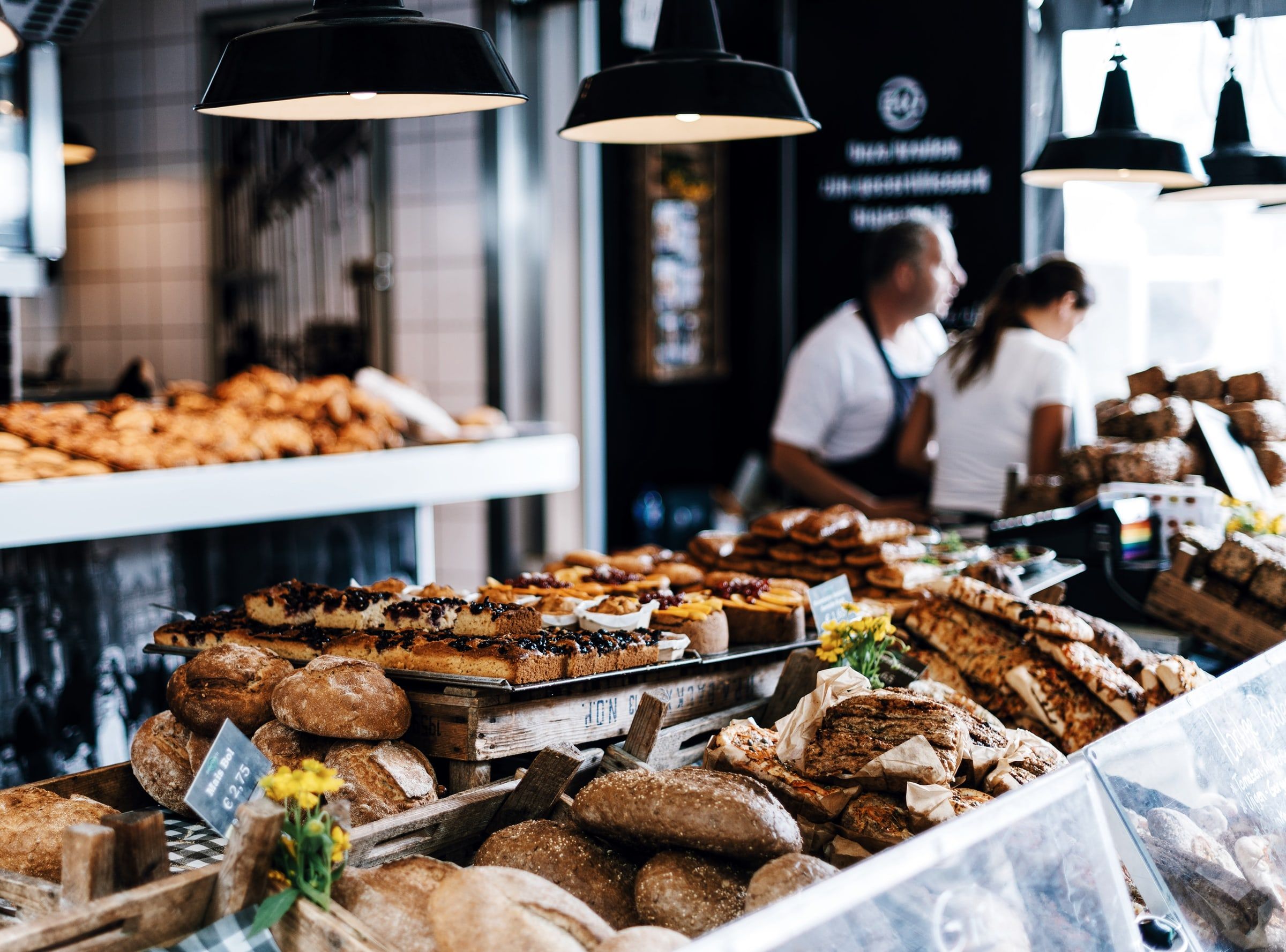 Mostrador de una panadería con hogazas, panes rústicos y bollería recién hecha, y los panaderos trabajando al fondo