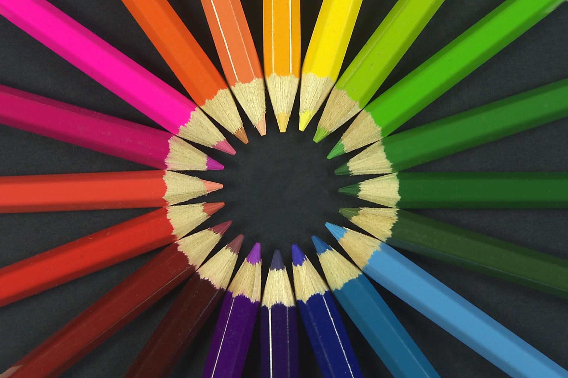 Lápices de colores colocados en círculo con las puntas hacia el centro, formando una rueda con todos los tonos