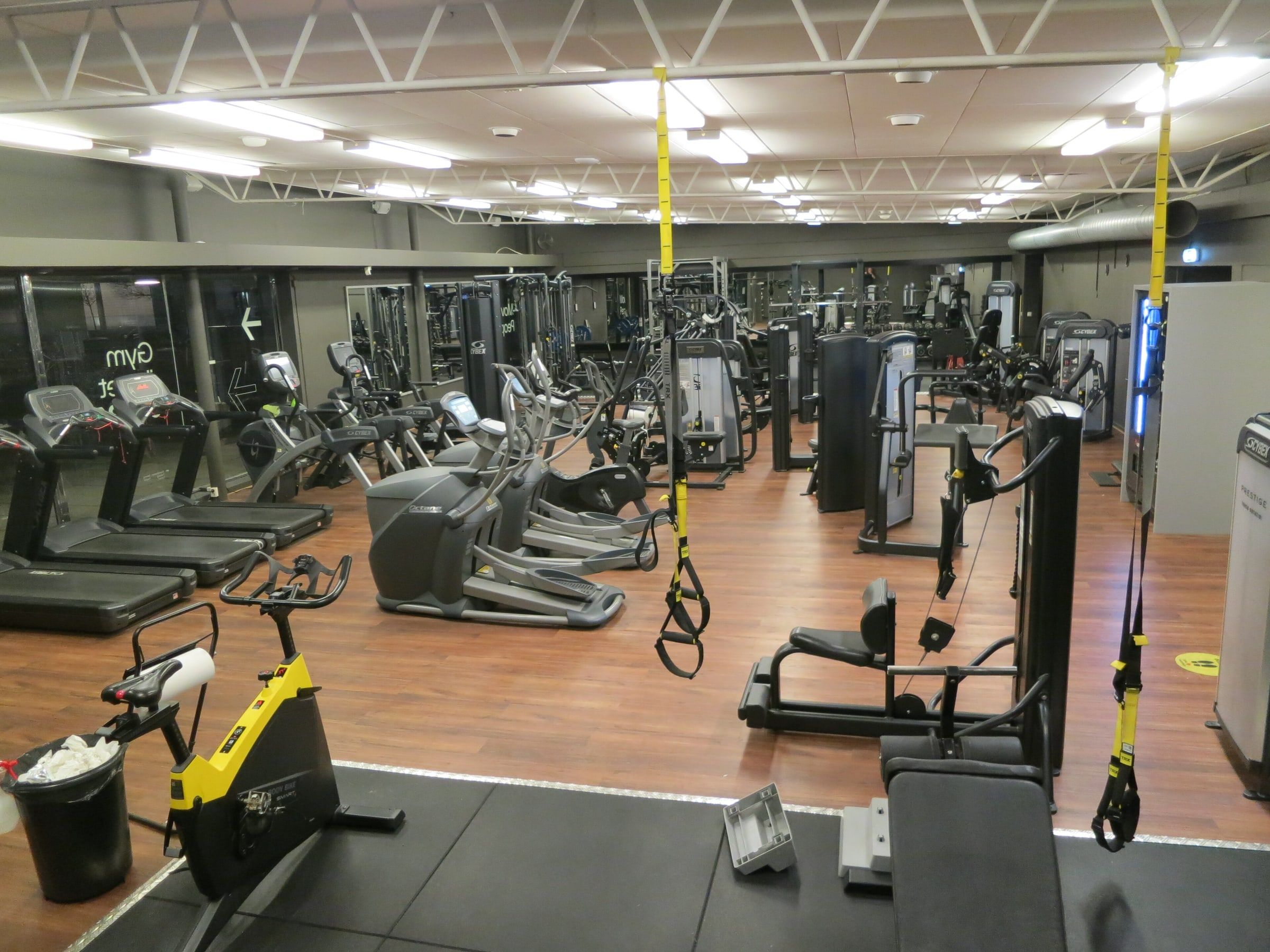 Sala de un gimnasio con cintas de correr, elípticas, bicicletas estáticas, máquinas de musculación y cintas de suspensión colgadas del techo