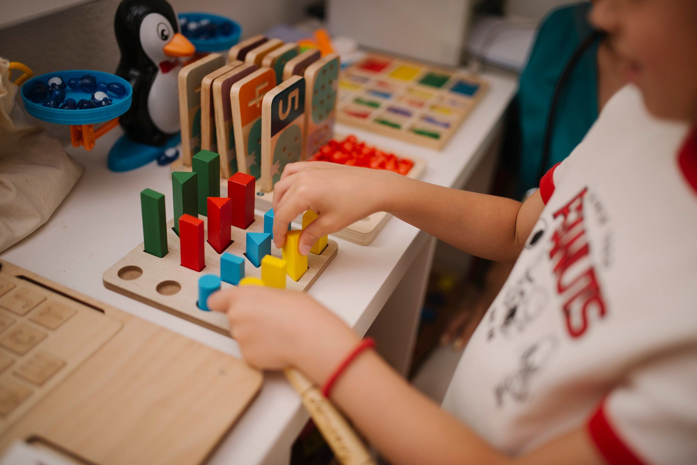 Niño pequeño jugando con piezas de madera de colores en una mesa llena de juguetes educativos