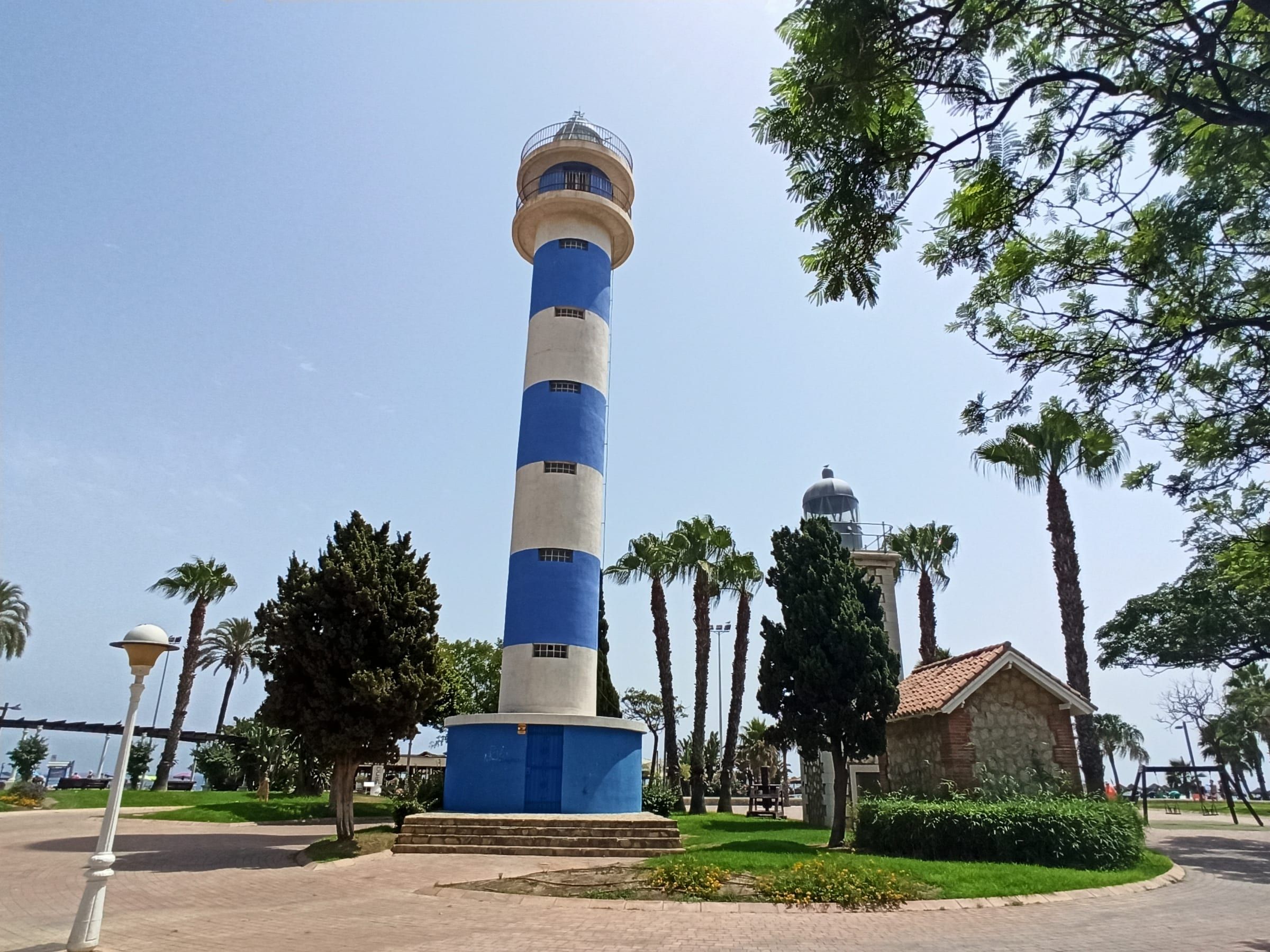 Faro de Torre del Mar de franjas azules y blancas entre palmeras