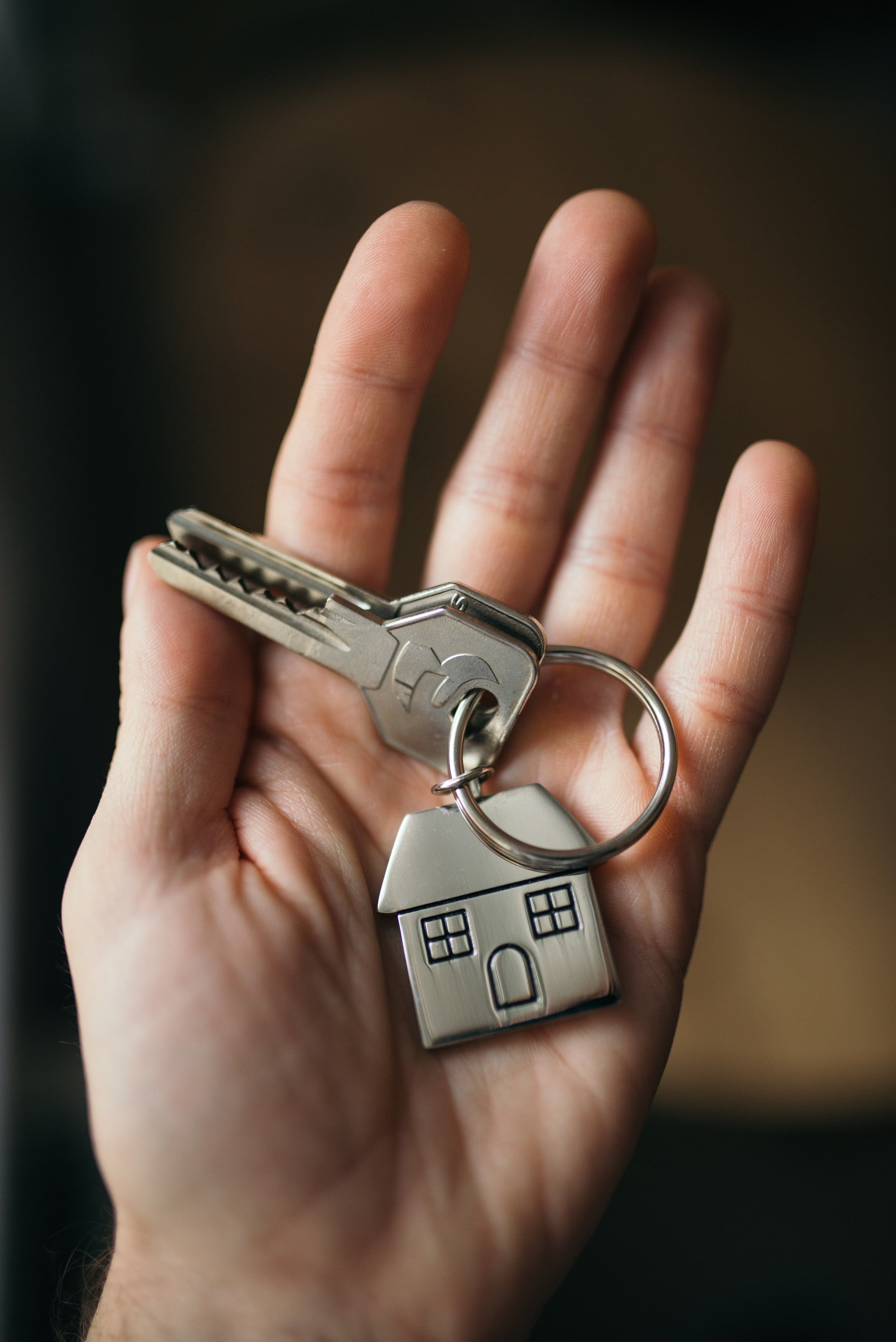 Mano abierta con las llaves de una vivienda colgadas de un llavero con forma de casa