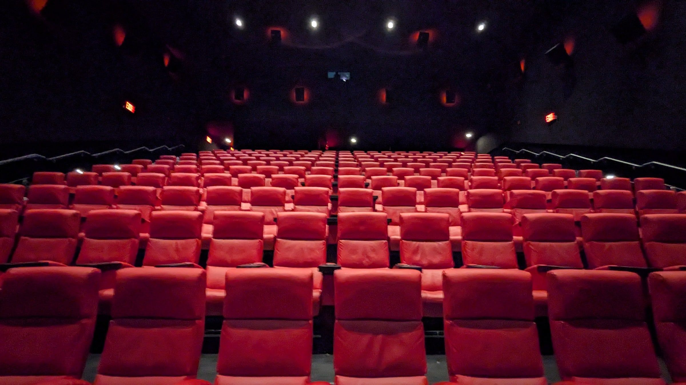 Sala de cine vacía con filas de butacas rojas escalonadas y pequeñas luces en el techo oscuro, a punto de empezar la sesión