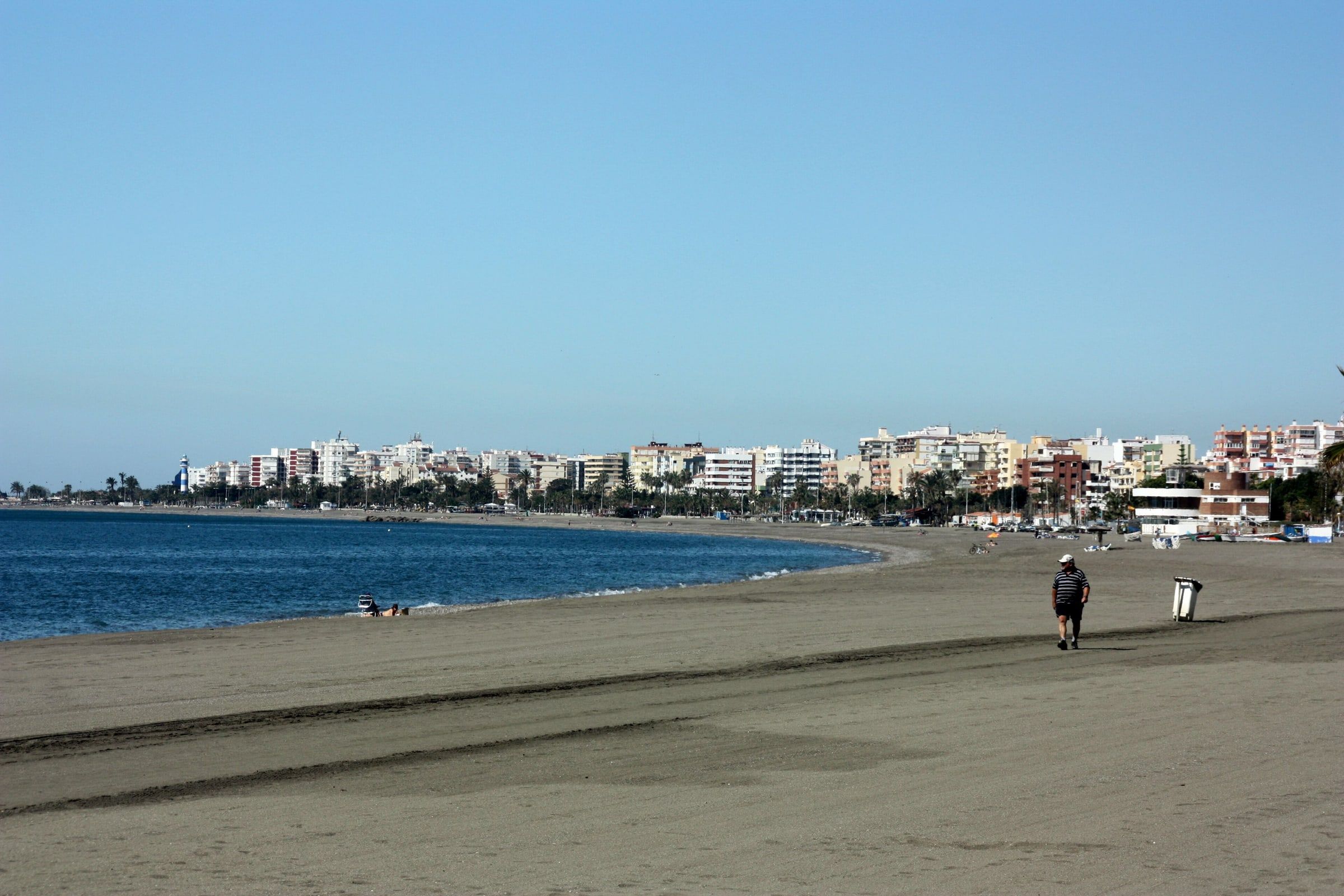 Vista de la playa de Torre del Mar desde el puerto de Caleta de Vélez, con la orilla, el mar en calma y los edificios del paseo al fondo