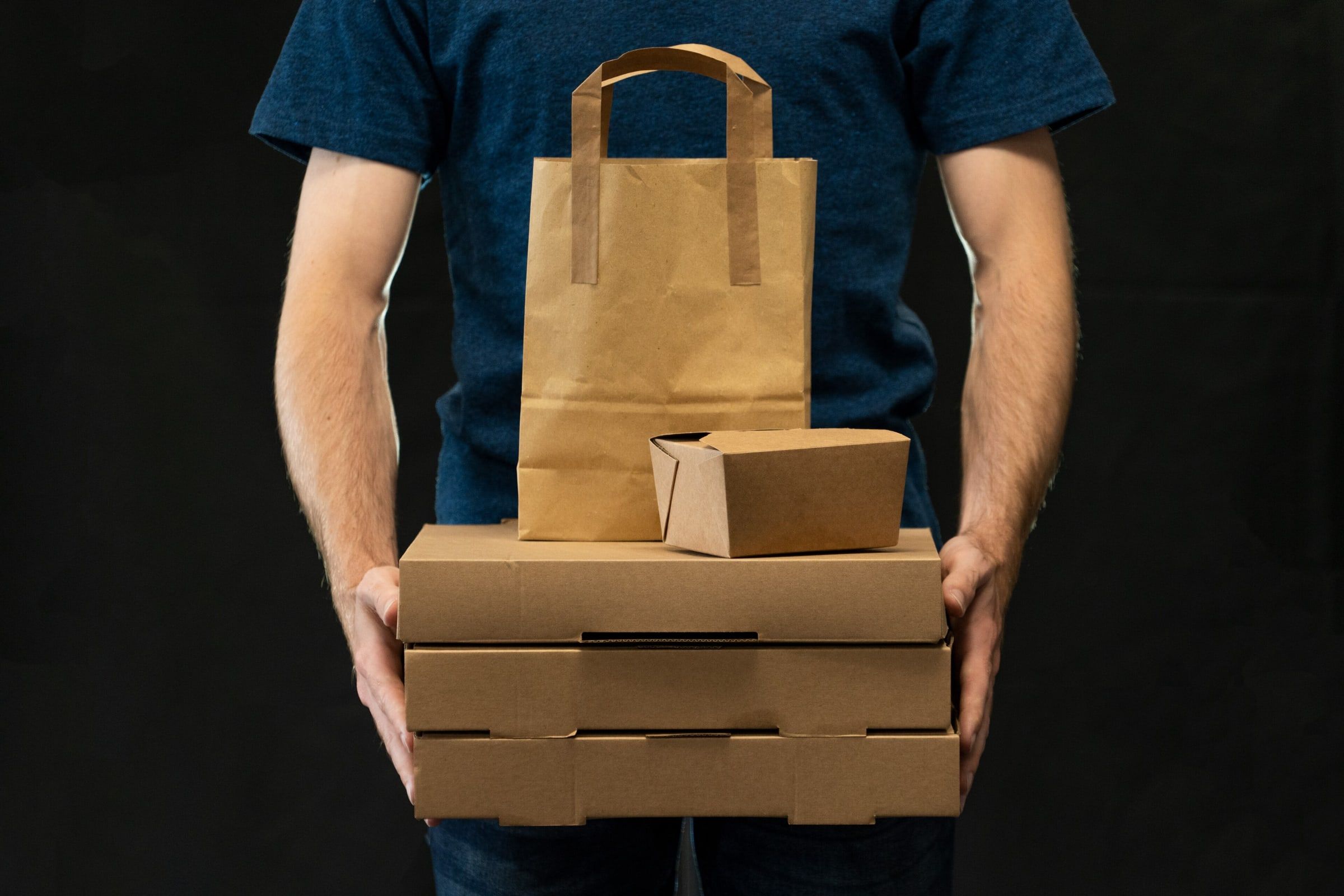 Repartidor sujetando una pila de cajas de pizza de cartón con una bolsa de papel encima, listo para entregar un pedido a domicilio