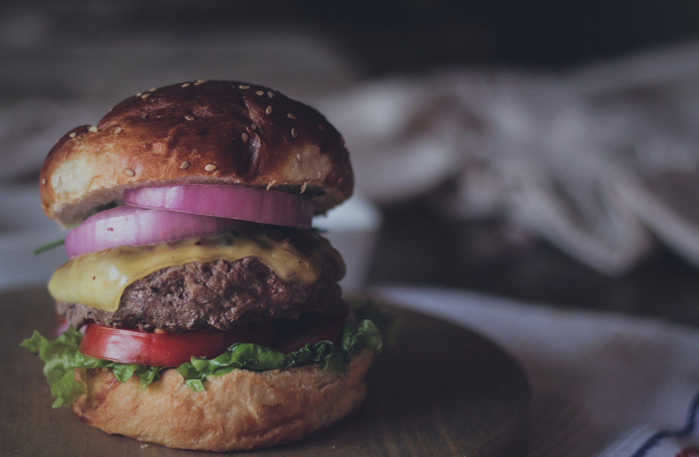Hamburguesa de carne con queso fundido, cebolla morada, tomate y lechuga en pan de brioche, sobre una tabla con fondo oscuro