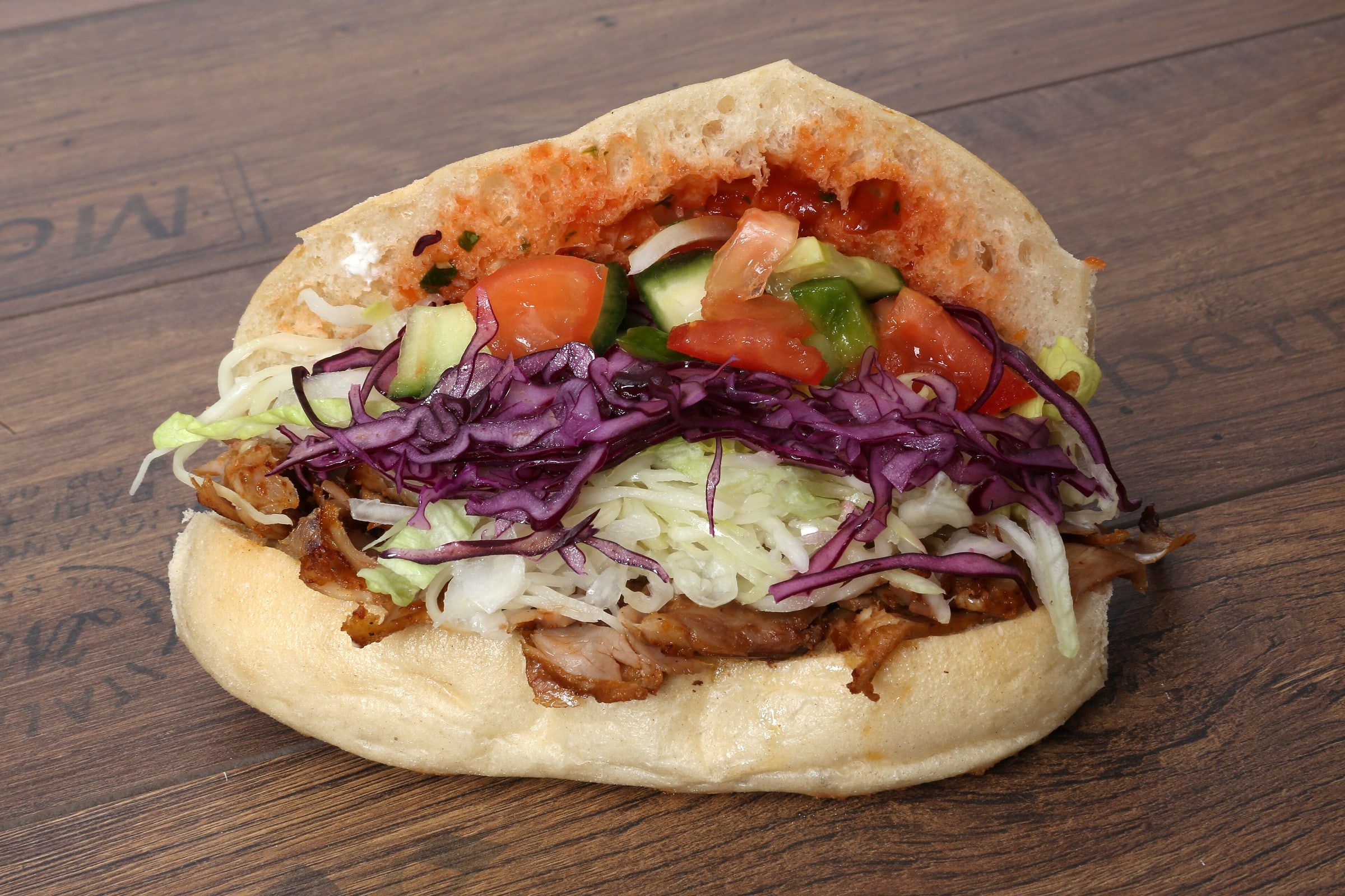 Döner kebab en pan de pita relleno de carne asada, lombarda, lechuga, tomate y pepino, sobre una mesa de madera