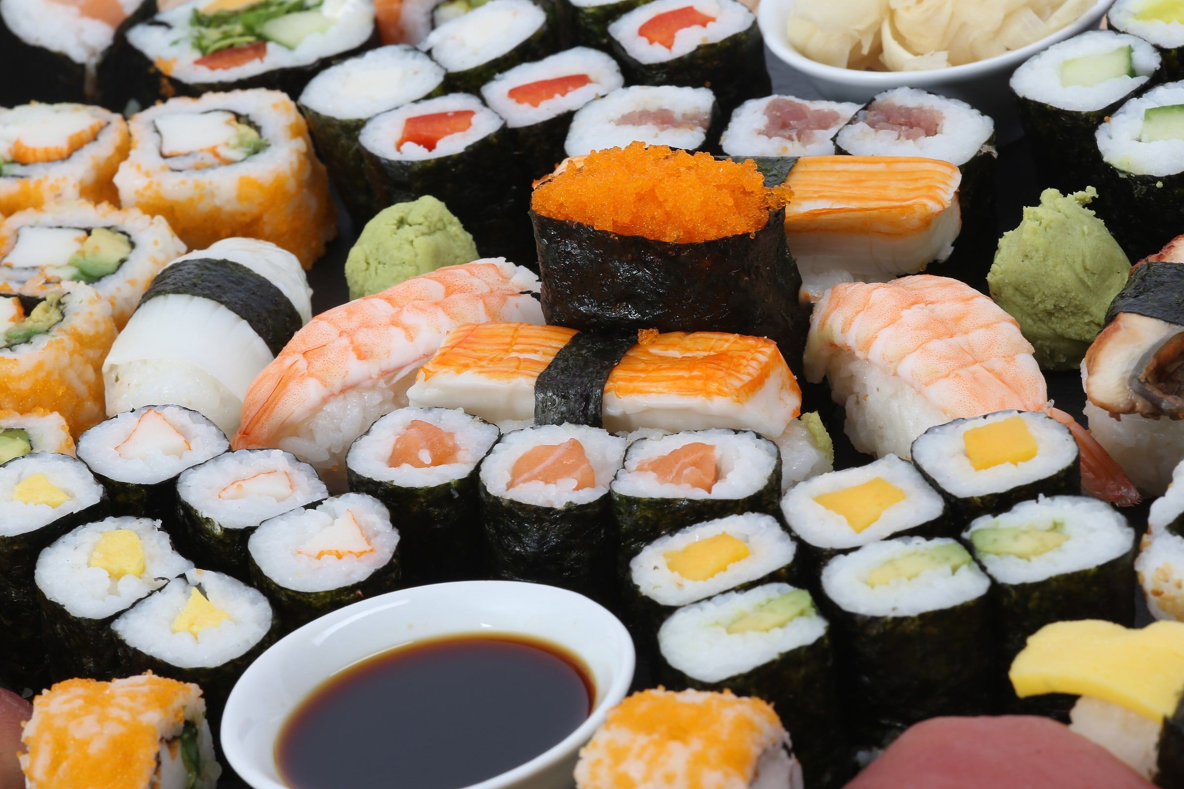 Bandeja de sushi variado con makis, nigiris de langostino y salmón, uramakis, wasabi y un cuenco de salsa de soja