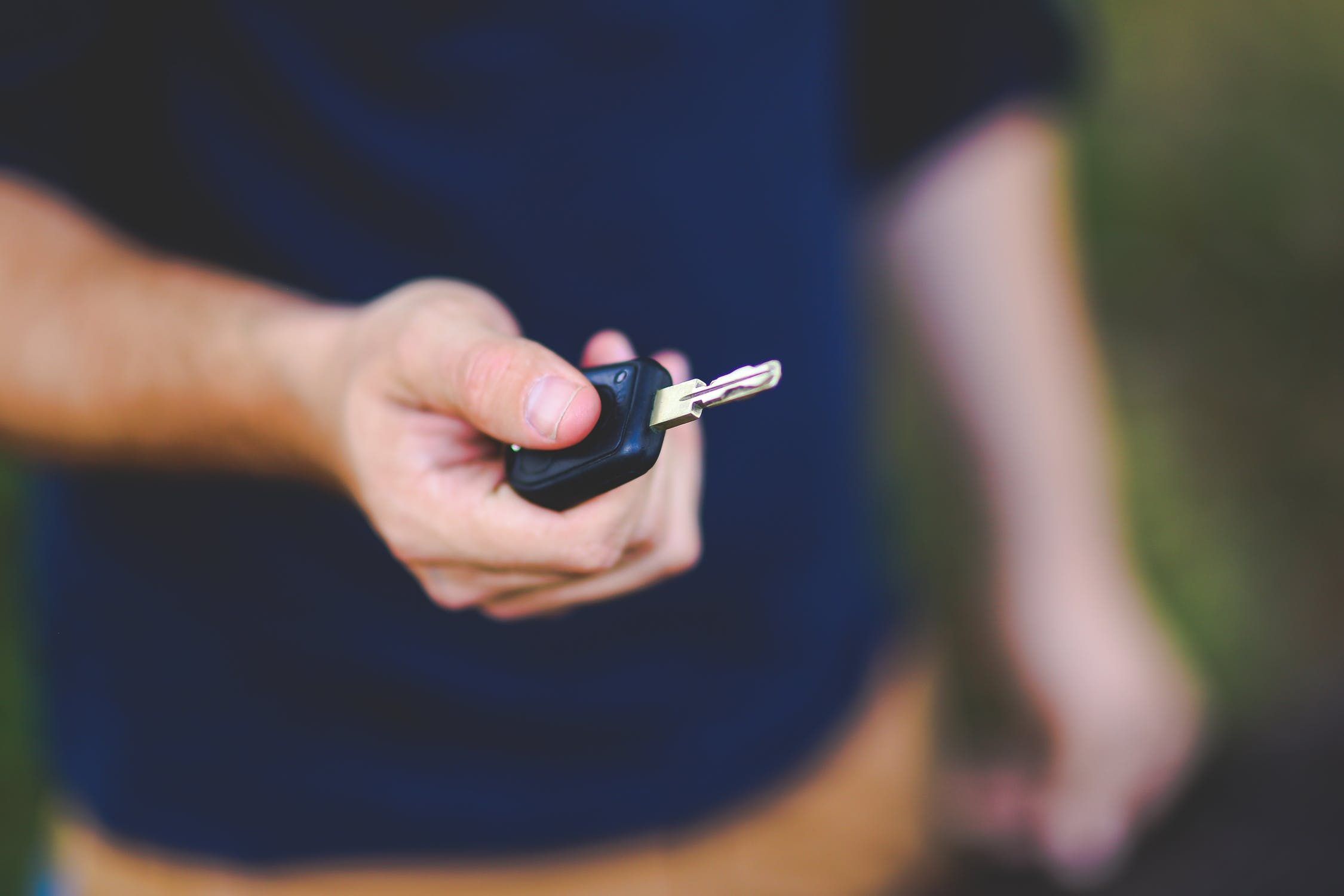 Mano que entrega la llave de un coche con mando a distancia, vista de cerca con el fondo desenfocado