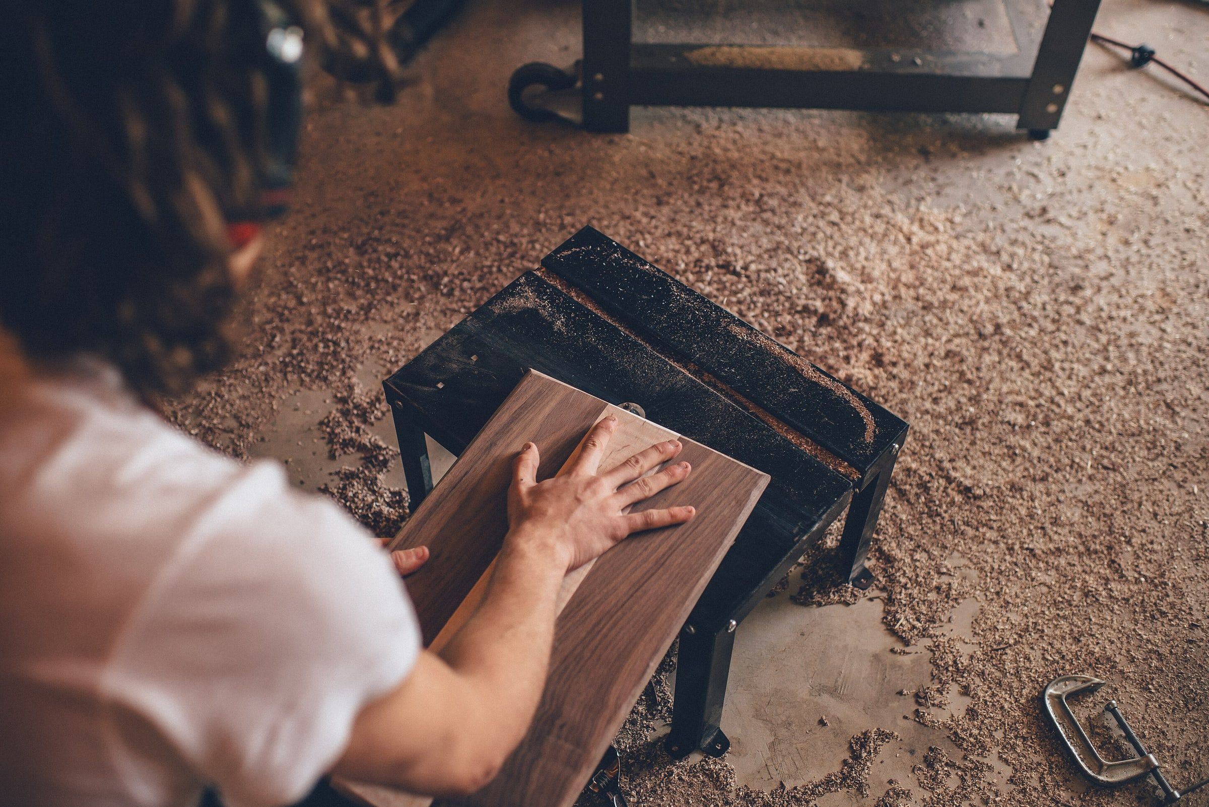 Persona trabajando a mano una tabla de madera en un taller de carpintería con el suelo cubierto de serrín