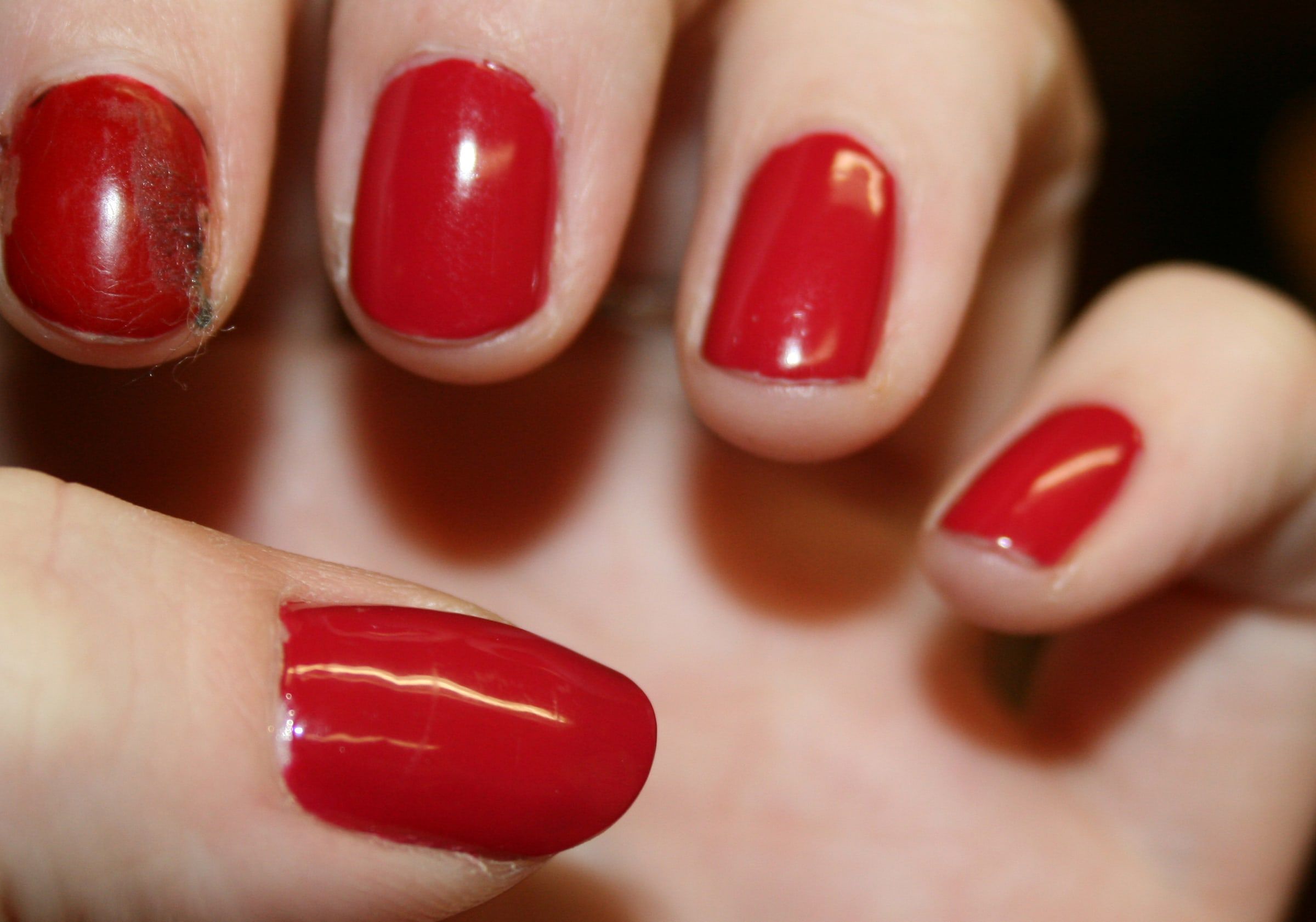 Mano con las uñas recién pintadas de esmalte rojo brillante, vista de cerca sobre un fondo cálido y desenfocado