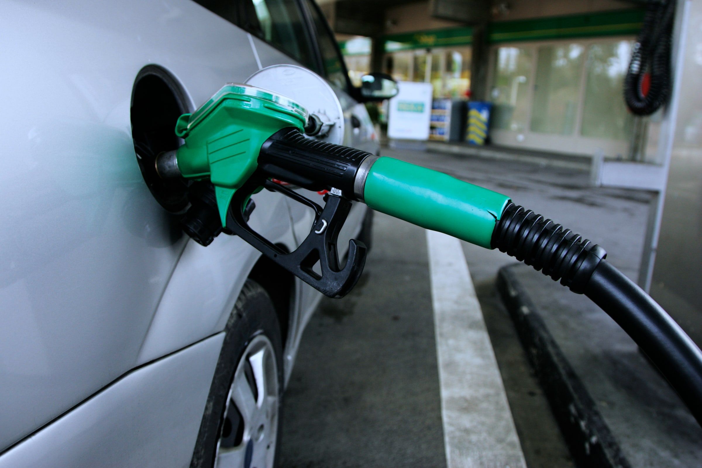 Pistola de repostaje verde metida en el depósito de un coche plateado junto al surtidor de una gasolinera