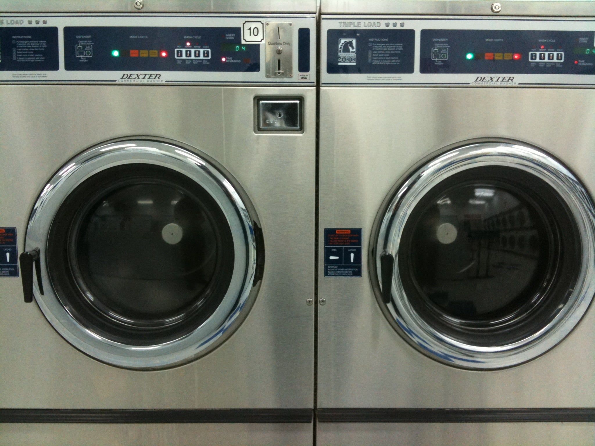Dos lavadoras industriales de acero inoxidable con su puerta redonda en una lavandería de autoservicio