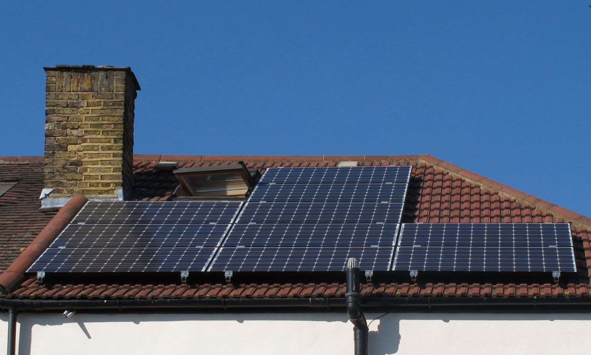 Placas solares fotovoltaicas recién instaladas sobre el tejado de tejas de una vivienda, bajo un cielo azul