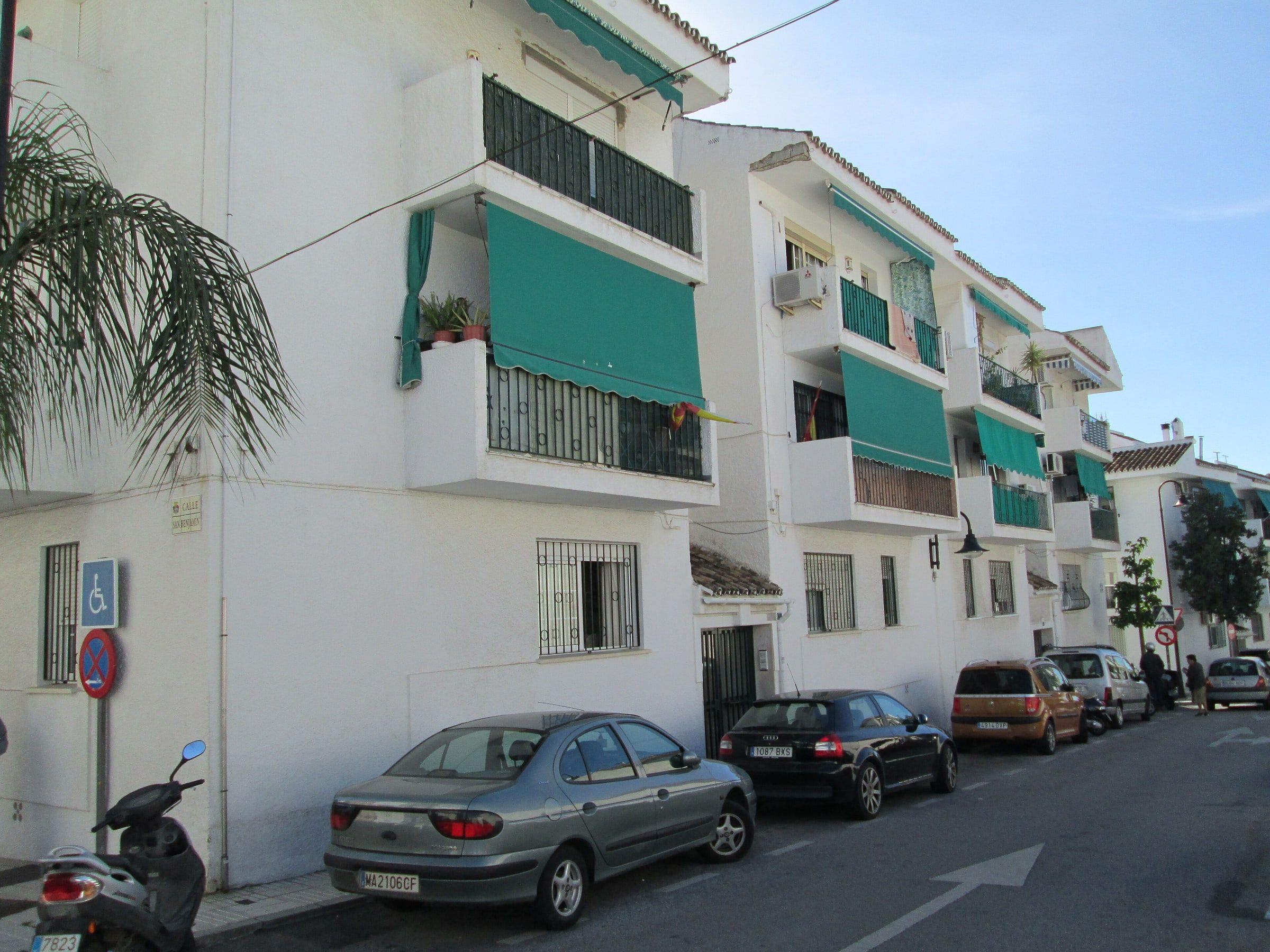 Calle de un pueblo de la Costa del Sol con edificios blancos y toldos verdes en balcones y ventanas